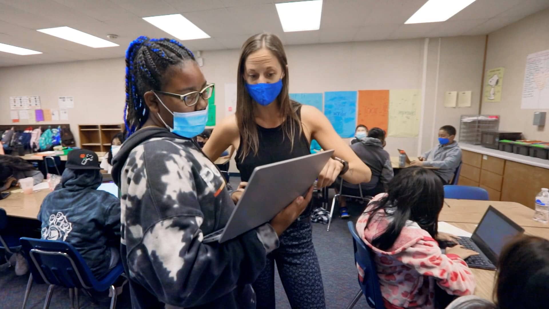 African american woman with mask pointing at laptop in the middle of a classroom