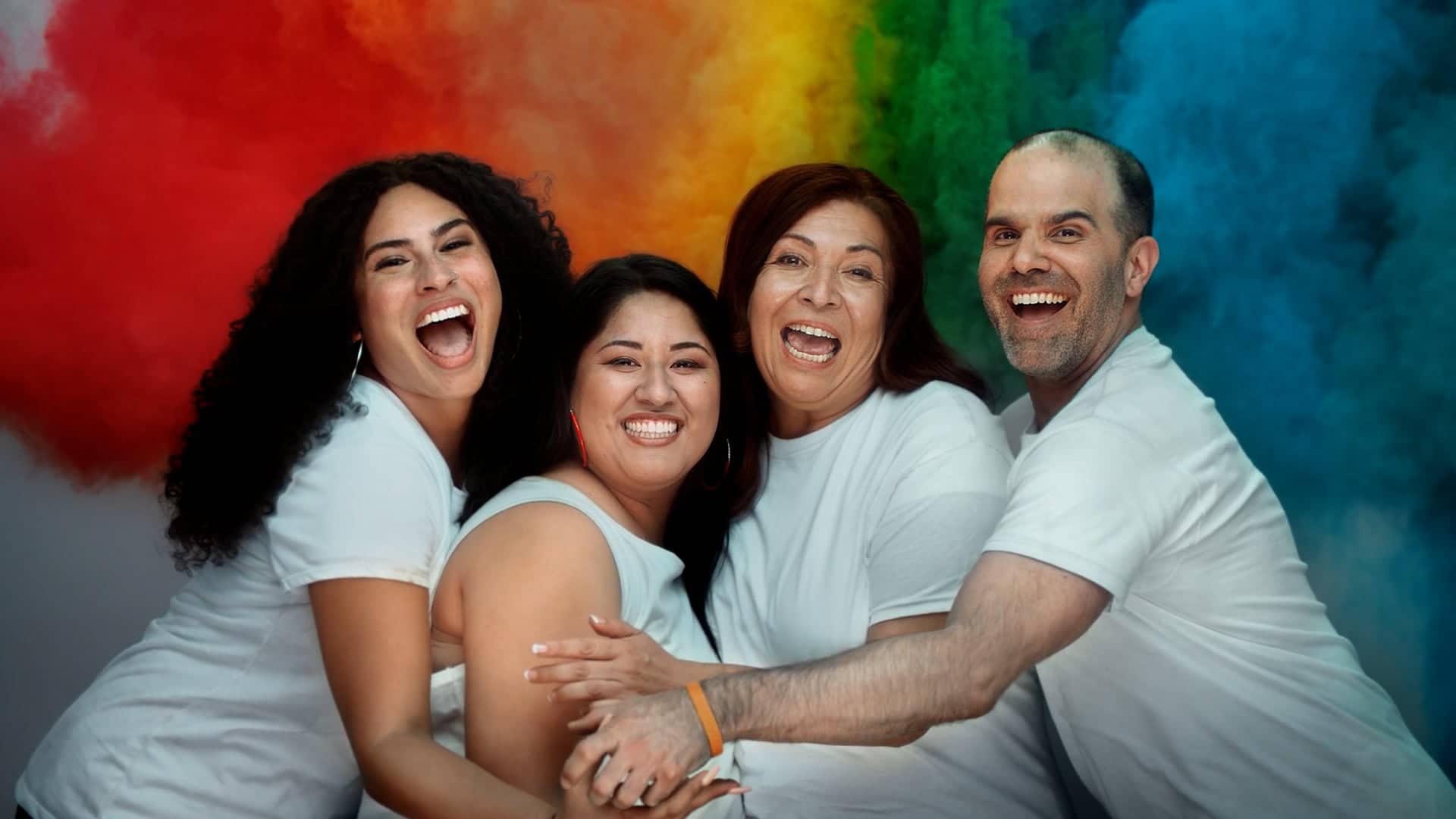 Four Latino people hug each other and smile proudly
